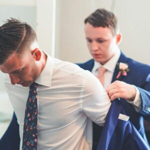 A groom gets assistance with his jacket from the best man on his wedding day.
